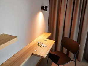 A modern room with a wooden desk, a chair, a wall-mounted light, and a curtain.