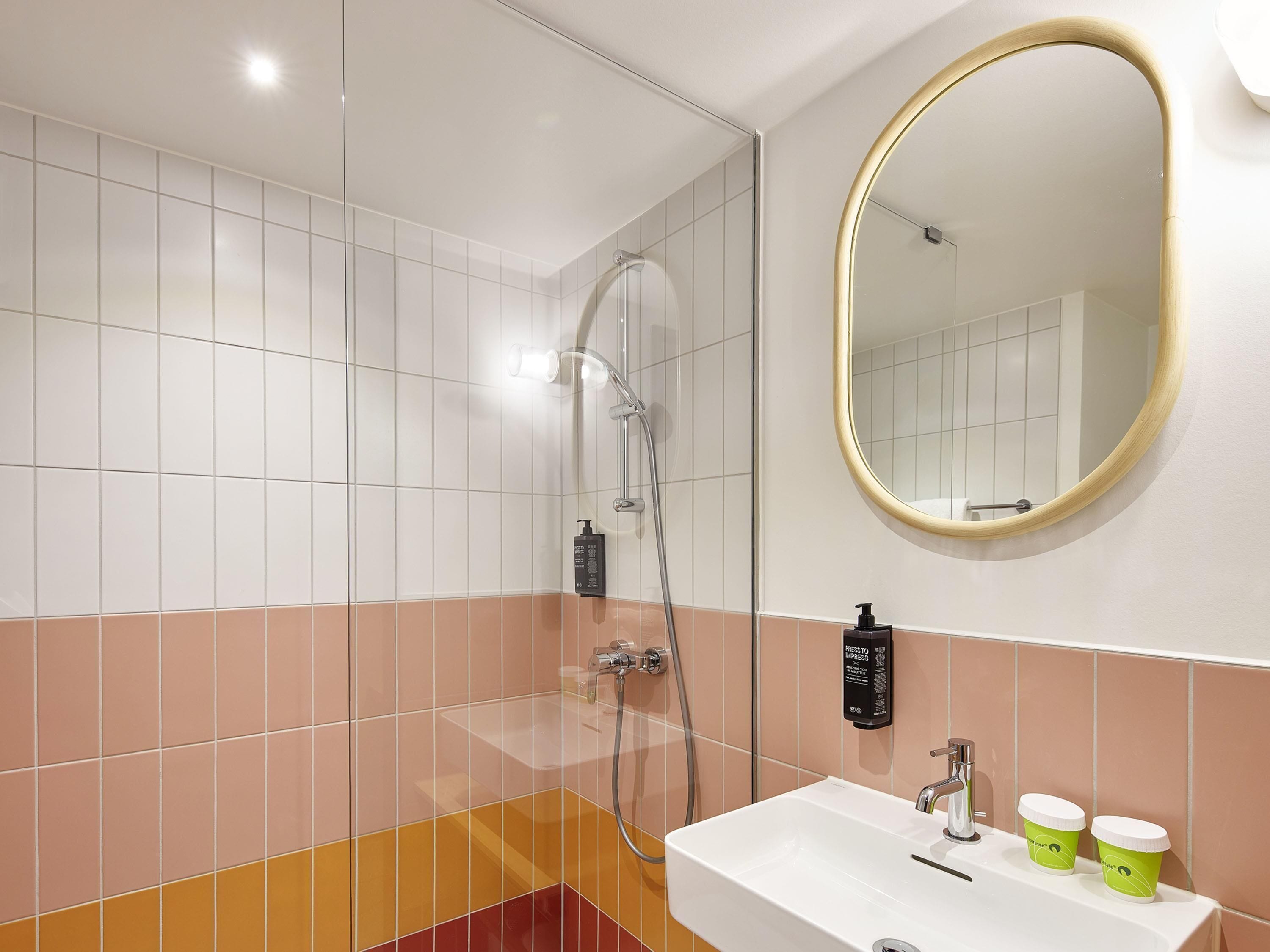 Un baño con ducha, lavamanos, espejo y una botella de champú.