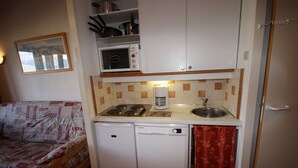 Cocina compacta con microondas, estufa, fregadero y lavavajillas. Un pequeño comedor con mesa y sofá.