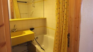 Un baño con puerta de madera, un lavamanos amarillo, un espejo y una bañera.