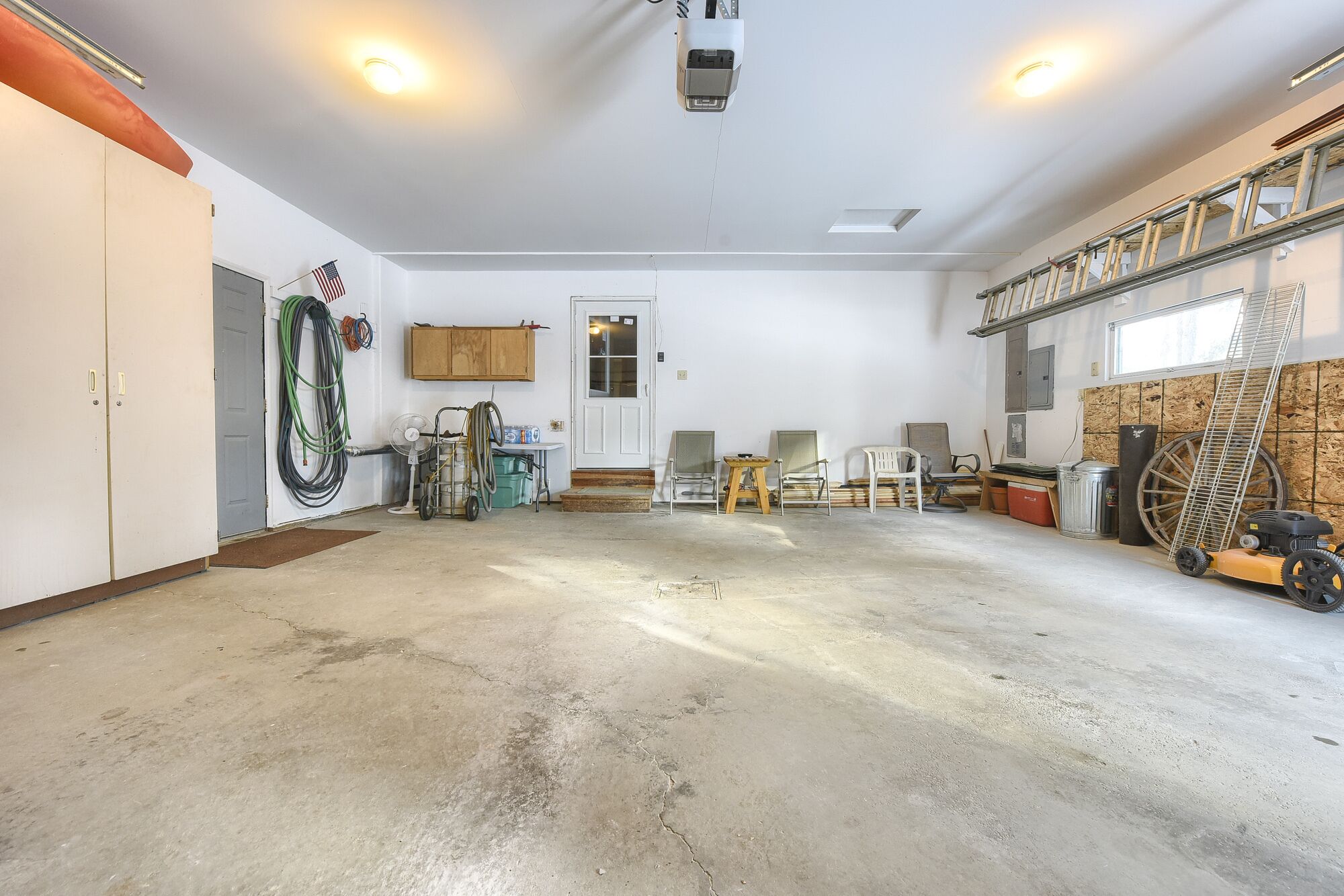 Uma garagem com piso de concreto, uma bancada de trabalho de madeira, um ventilador e uma escada.