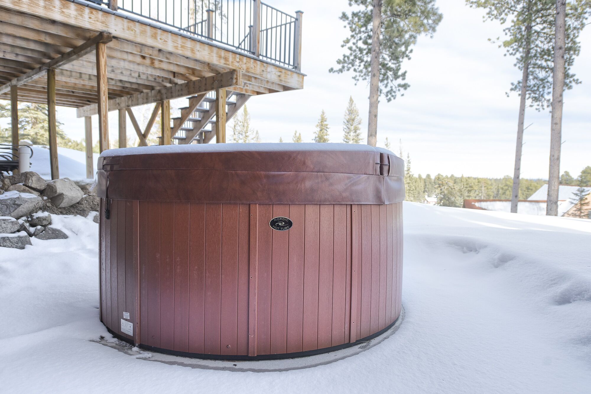 Een hottub in een besneeuwde omgeving, met een houten terras en een trap die naar een overdekt gedeelte leidt.
