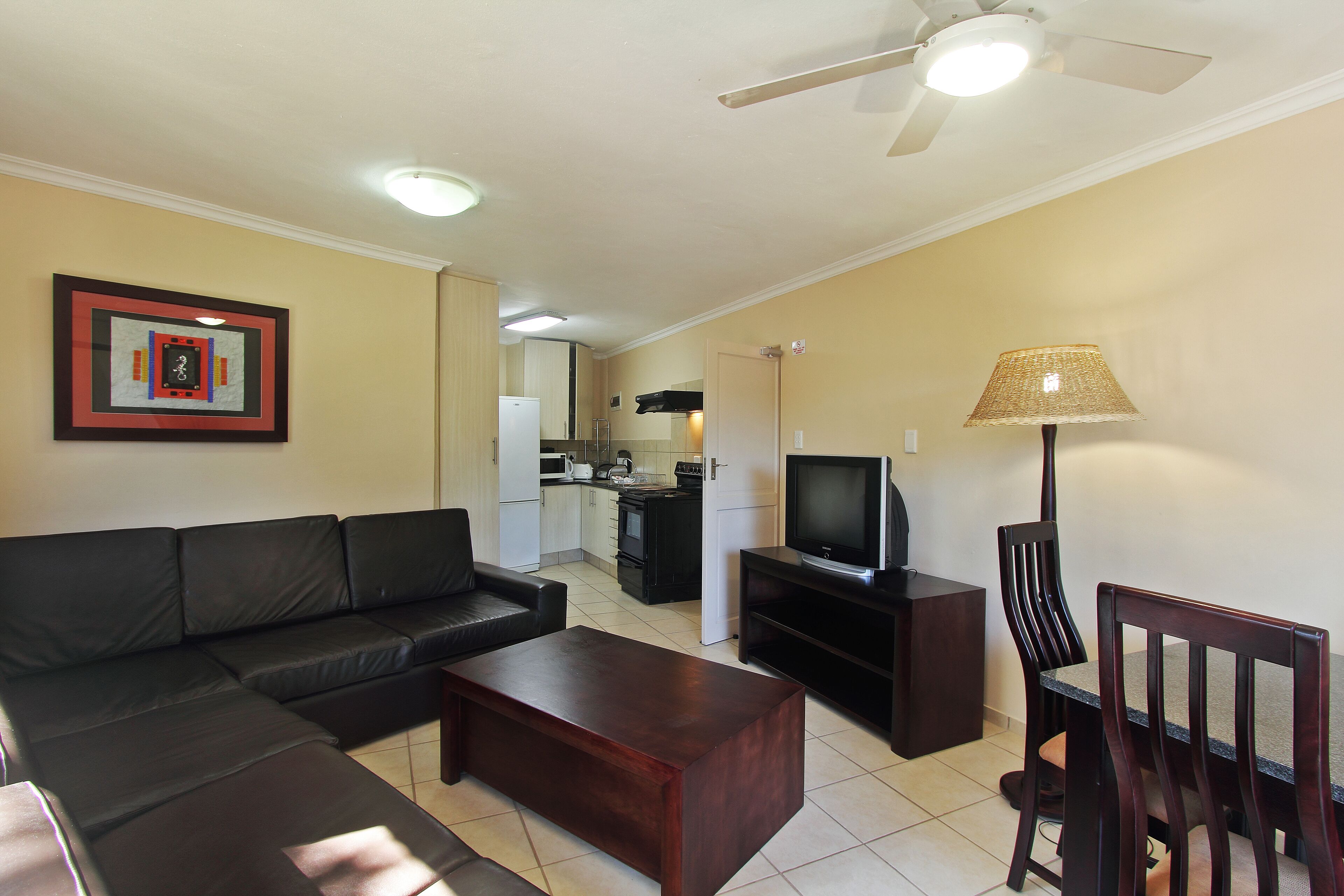 A living room with a sofa, coffee table, TV stand, and a dining area with chairs.