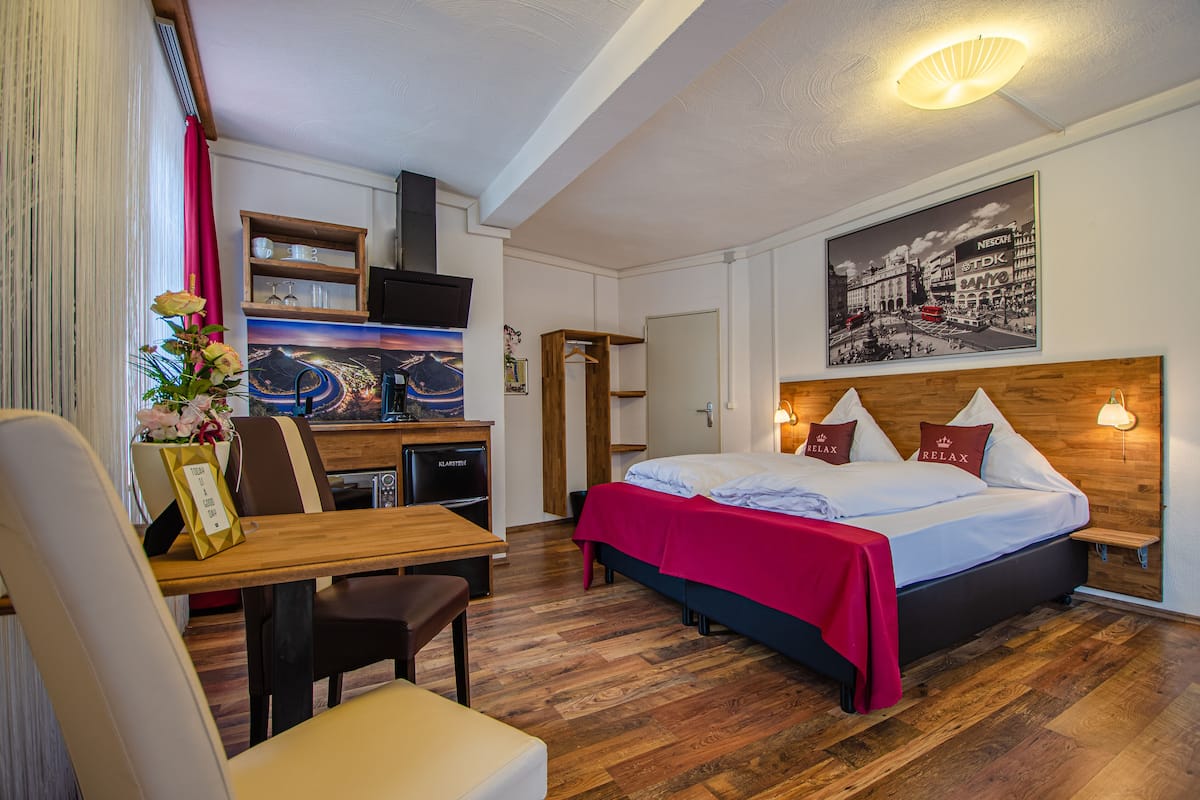 Ein Hotelzimmer mit einem Bett, einem Schreibtisch und einem Stuhl. An der Wand hängt ein Gemälde und es gibt ein Fenster mit Vorhängen.