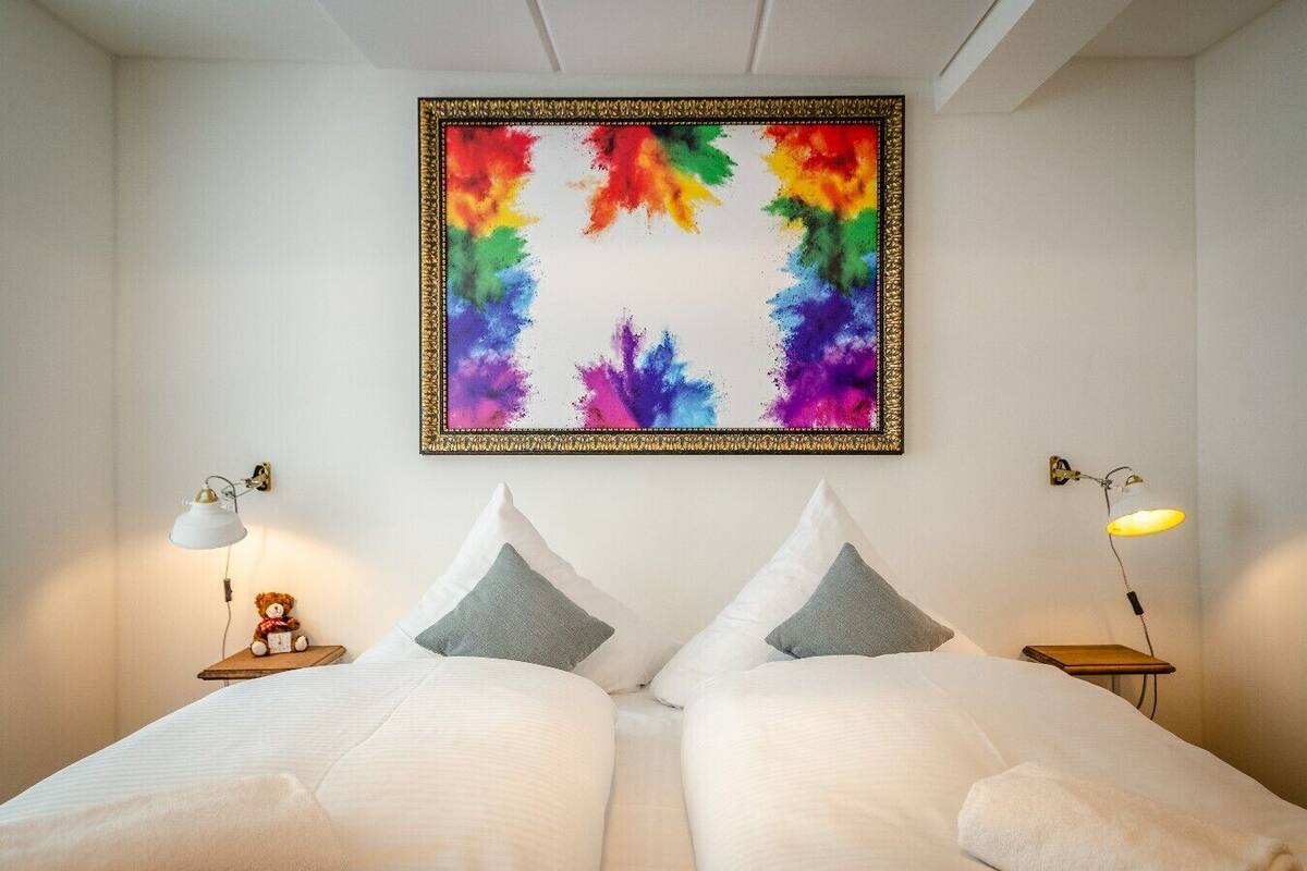 Ein Schlafzimmer mit einem Bett, zwei Kissen, einem farbenfrohen abstrakten Gemälde und zwei Nachttischlampen.