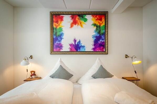 Un dormitorio con una cama, dos almohadas, un cuadro abstracto colorido y dos lámparas de noche.