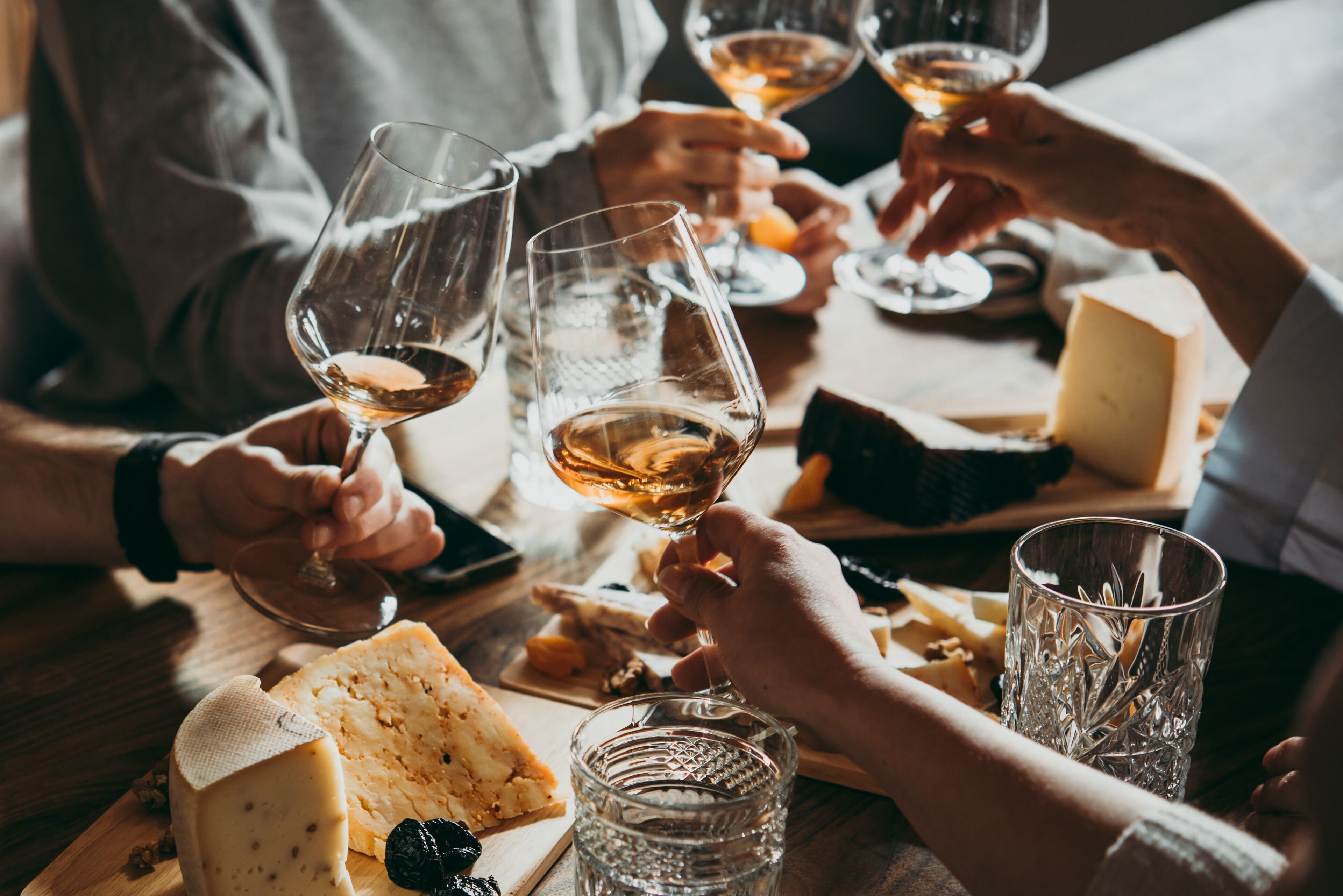 A group of people toasting with wine glasses at a table with cheese and bread.