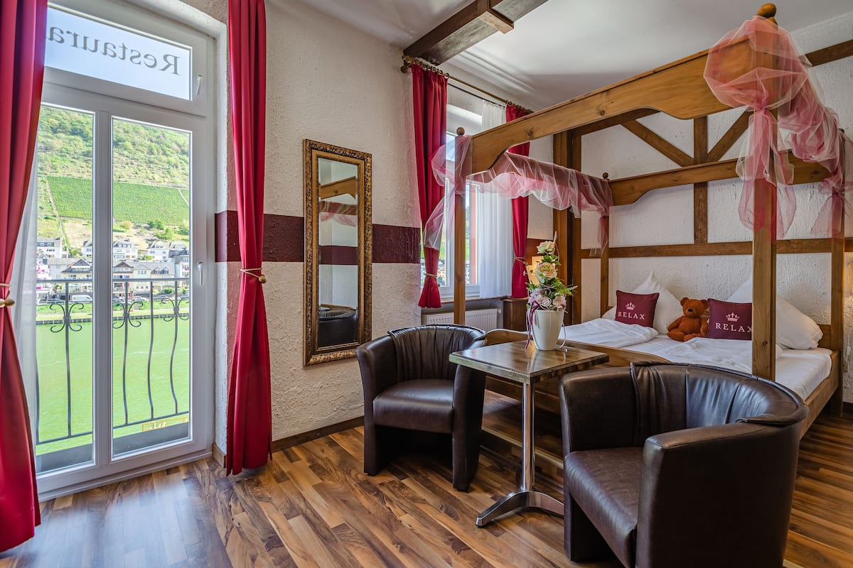 Ein Zimmer mit einem Bett, zwei Stühlen, einem Tisch, einem Spiegel und Blick auf eine grüne Landschaft durch ein Fenster.