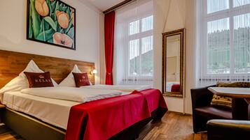 A hotel room with a large bed, a red bedspread, a painting of tulips, a mirror, and a view of trees through the window.