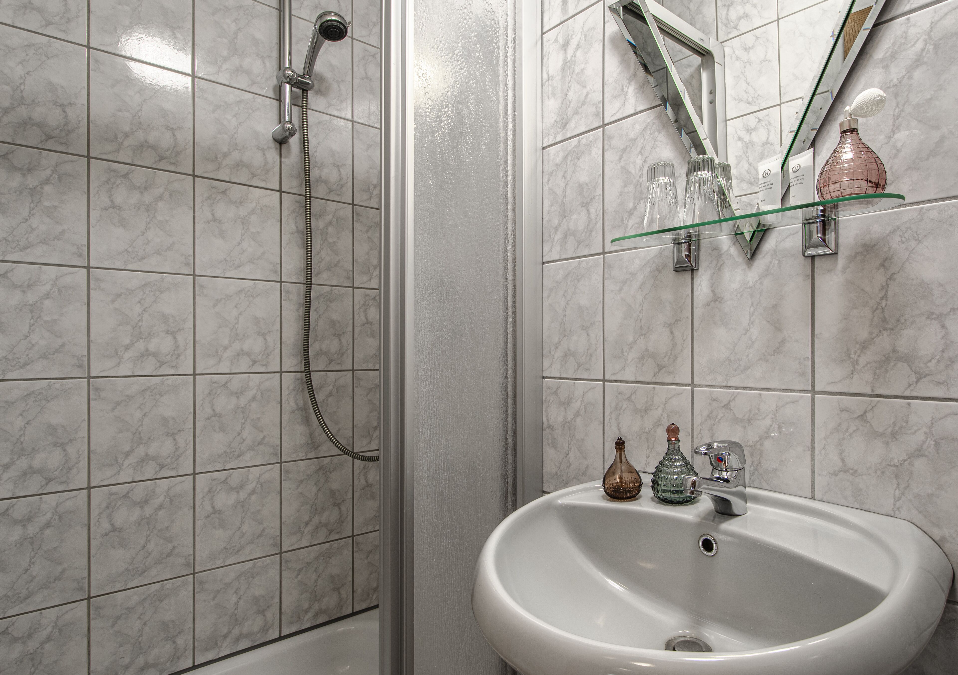 Une salle de bain avec une douche, un lavabo et une étagère en verre où sont rangés les articles de toilette.