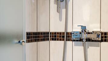 Eine Dusche mit Handbrause und flexiblem Duschschlauch, vor einer gefliesten Wand mit dekorativer Bordüre.