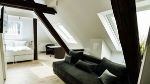 Ein modernes Schlafzimmer im Loft-Stil mit schrägem Dach, einem Bett, einem dunkelgrauen Sofa und einem kleinen Tisch.