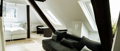 A modern loft bedroom with a sloped ceiling, a bed, a dark grey sofa, and a small table.