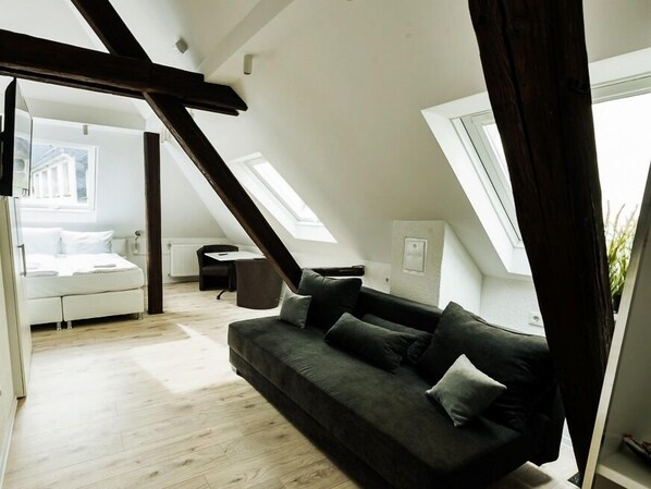 A modern loft bedroom with a sloped ceiling, a bed, a dark grey sofa, and a small table.