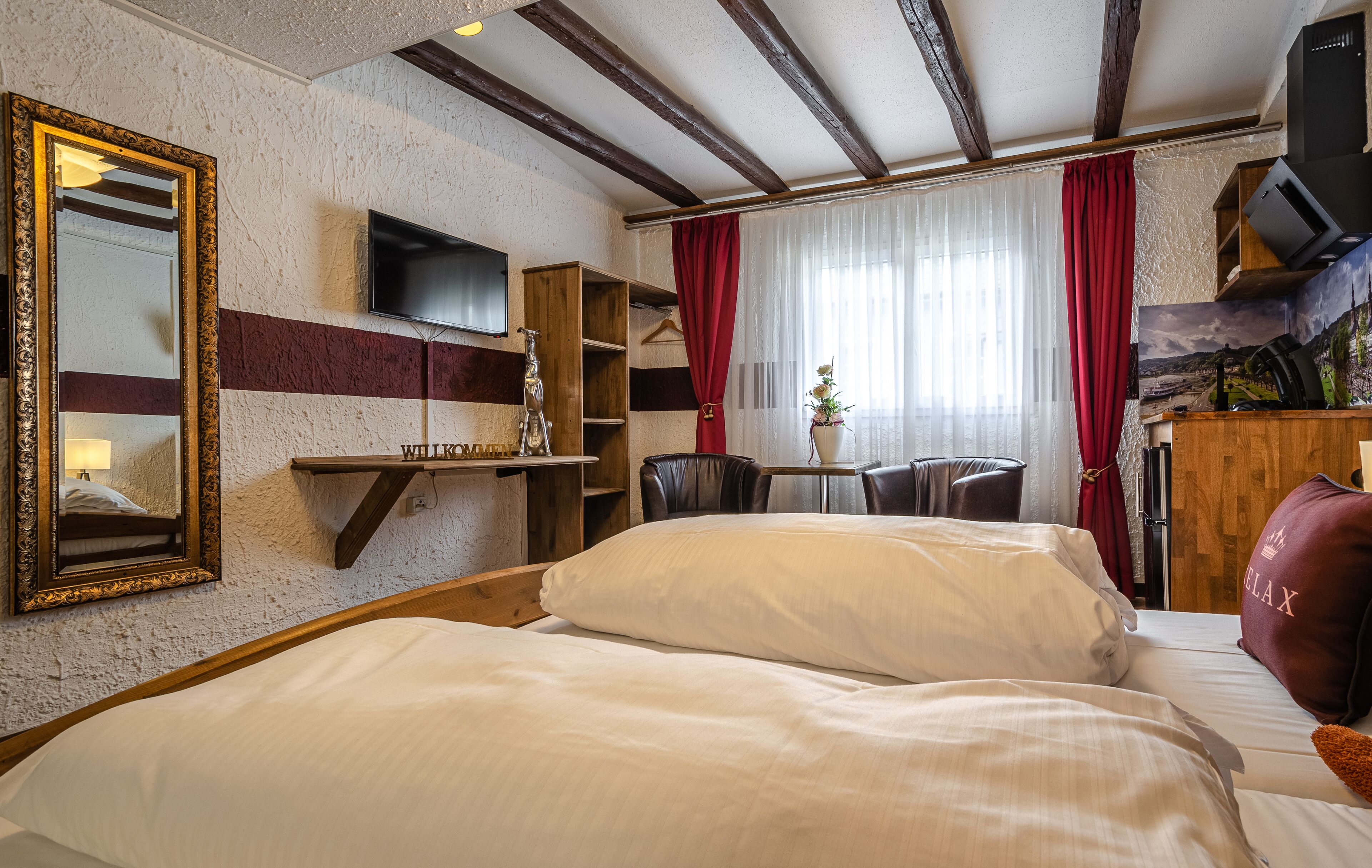 A hotel room with a large bed, a TV mounted on the wall, a wooden shelf, and a desk with a chair.