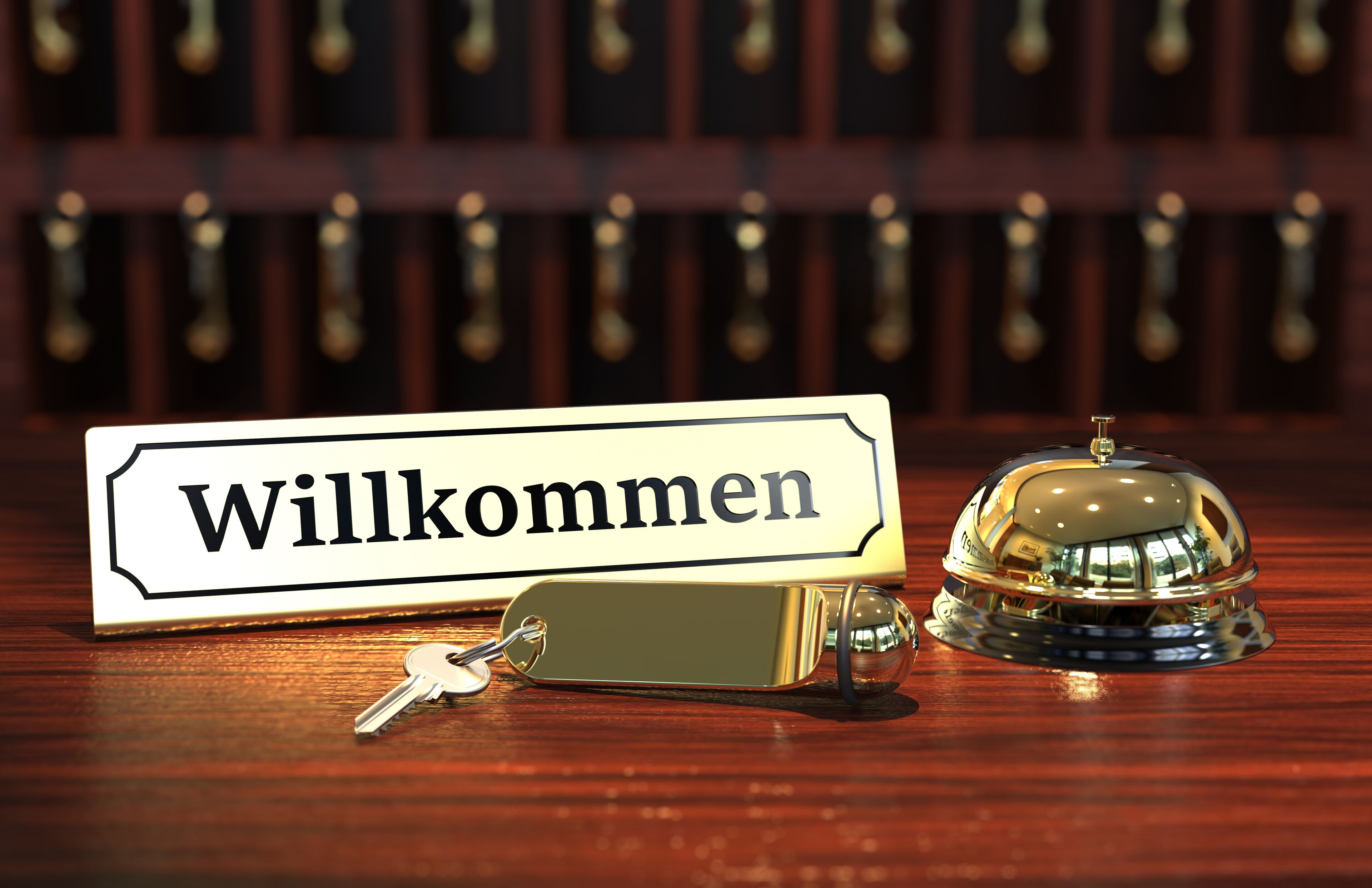 Zona de recepción de un hotel con un cartel de 'Willkommen', un timbre y llaves sobre una mesa de madera.