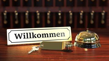 Zona de recepción de un hotel con un cartel de 'Willkommen', un timbre y llaves sobre una mesa de madera.