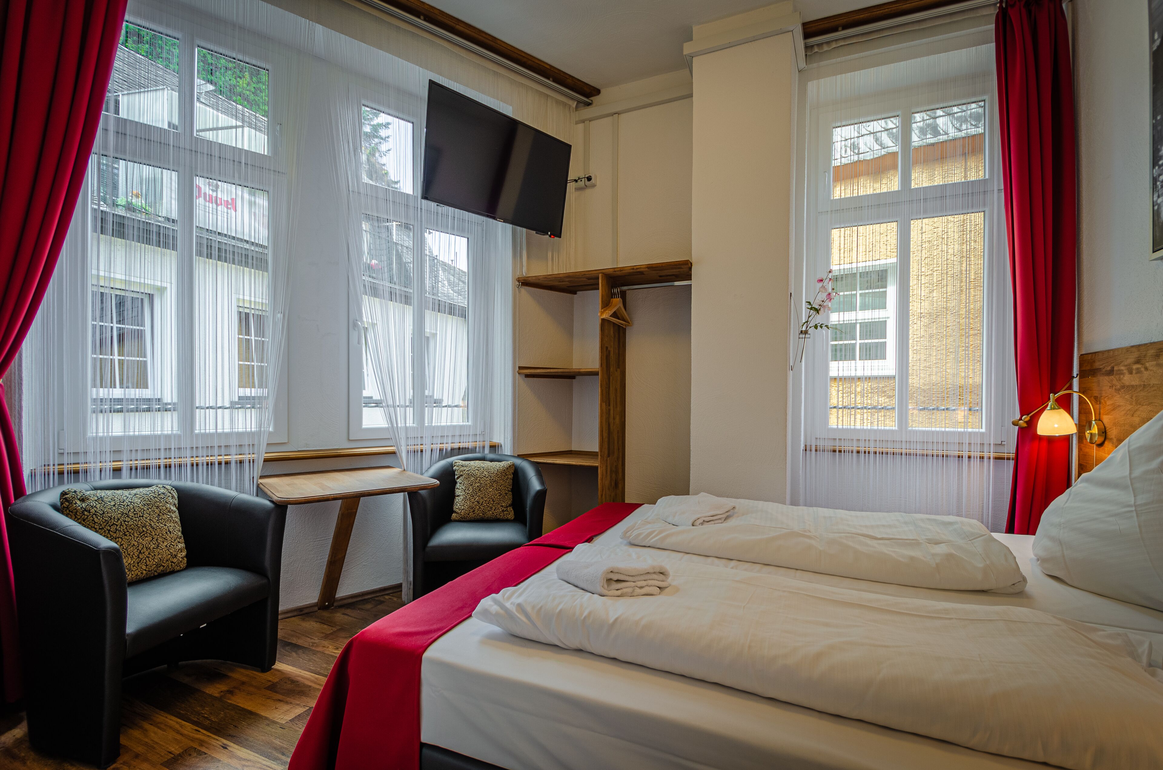 Habitación de hotel con cama, dos sillas, escritorio, televisor y ventana con cortinas.