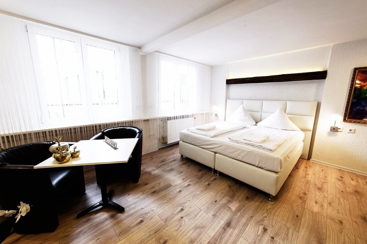 Ein modernes Hotelzimmer mit einem großen Bett, einem Esstisch und einem schwarzen Ledersessel.