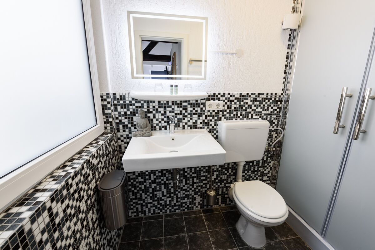 A compact bathroom with a white sink, black and white checkered tiles, a toilet, and a small trash bin.