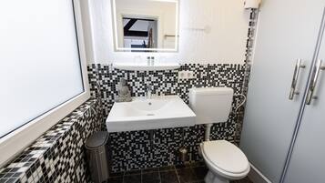 A compact bathroom with a white sink, black and white checkered tiles, a toilet, and a small trash bin.