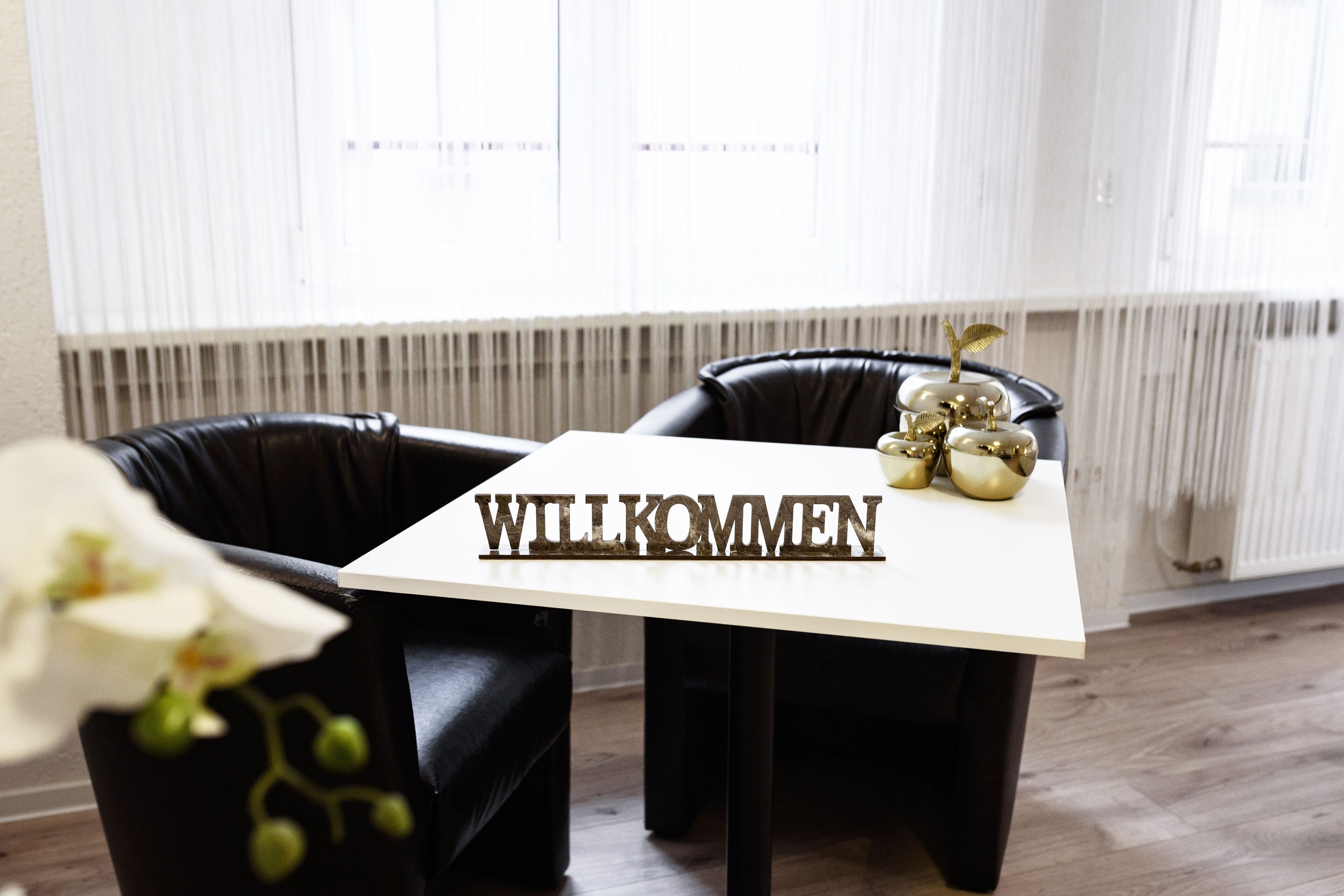 Ein modernes Zimmer mit einem weißen Tisch, auf dem das Wort 'WILLKOMMEN' steht, und einer dekorativen Anordnung goldener Ornamente.