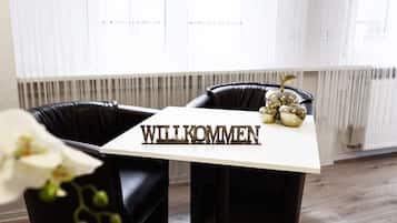 Ein modernes Zimmer mit einem weißen Tisch, auf dem das Wort 'WILLKOMMEN' steht, und einer dekorativen Anordnung goldener Ornamente.