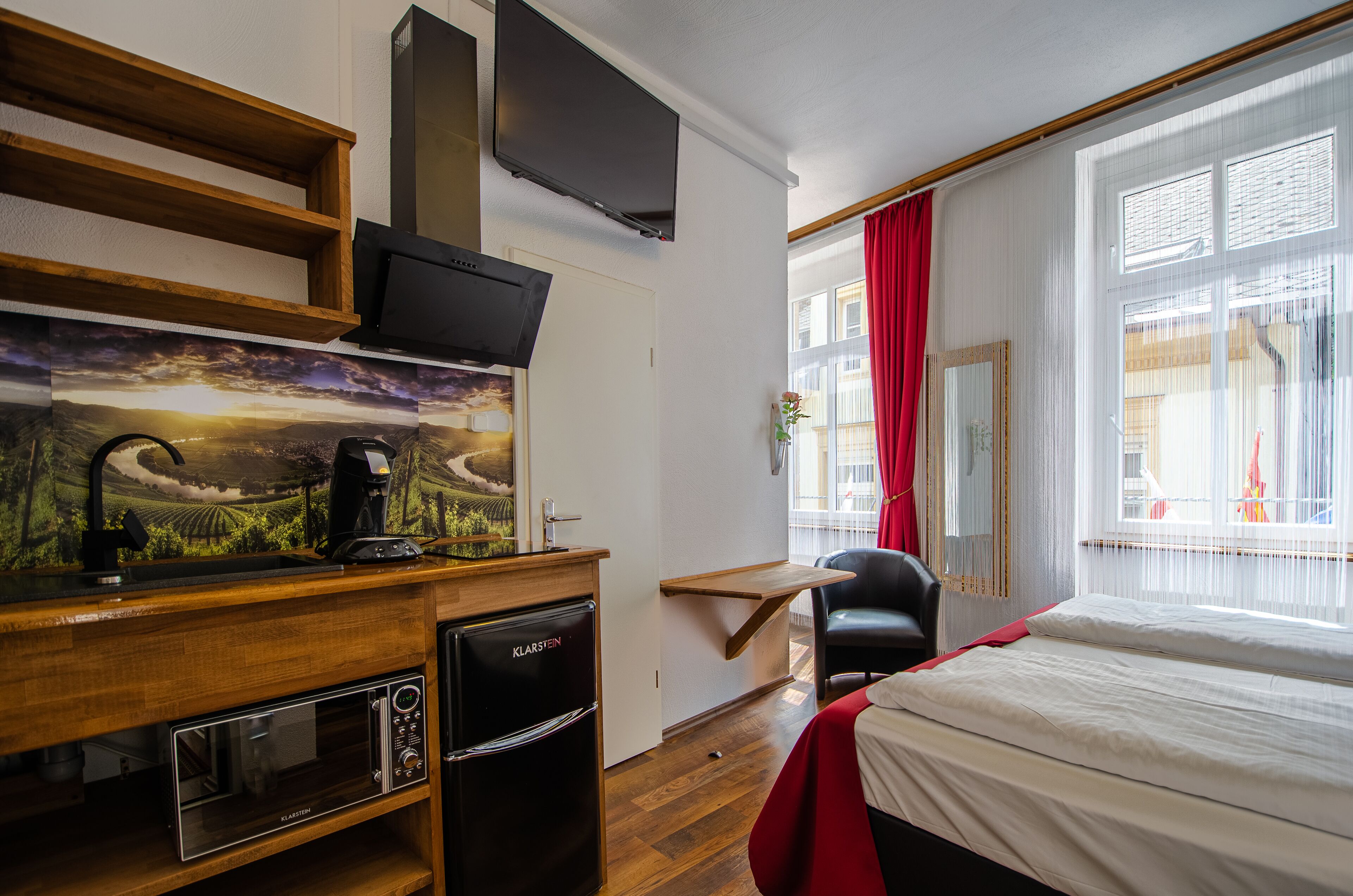 A hotel room with a bed, a desk with a coffee machine, a TV, and a window with curtains.