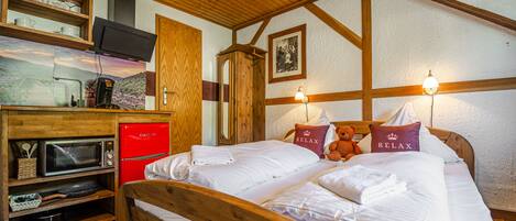 A bedroom with a wooden bed, two pillows with 'RELAX' text, a red appliance, and a wooden shelf with kitchen items.