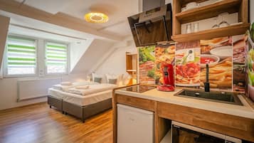 A compact bedroom with a bed, a small kitchenette, and a window with blinds.
