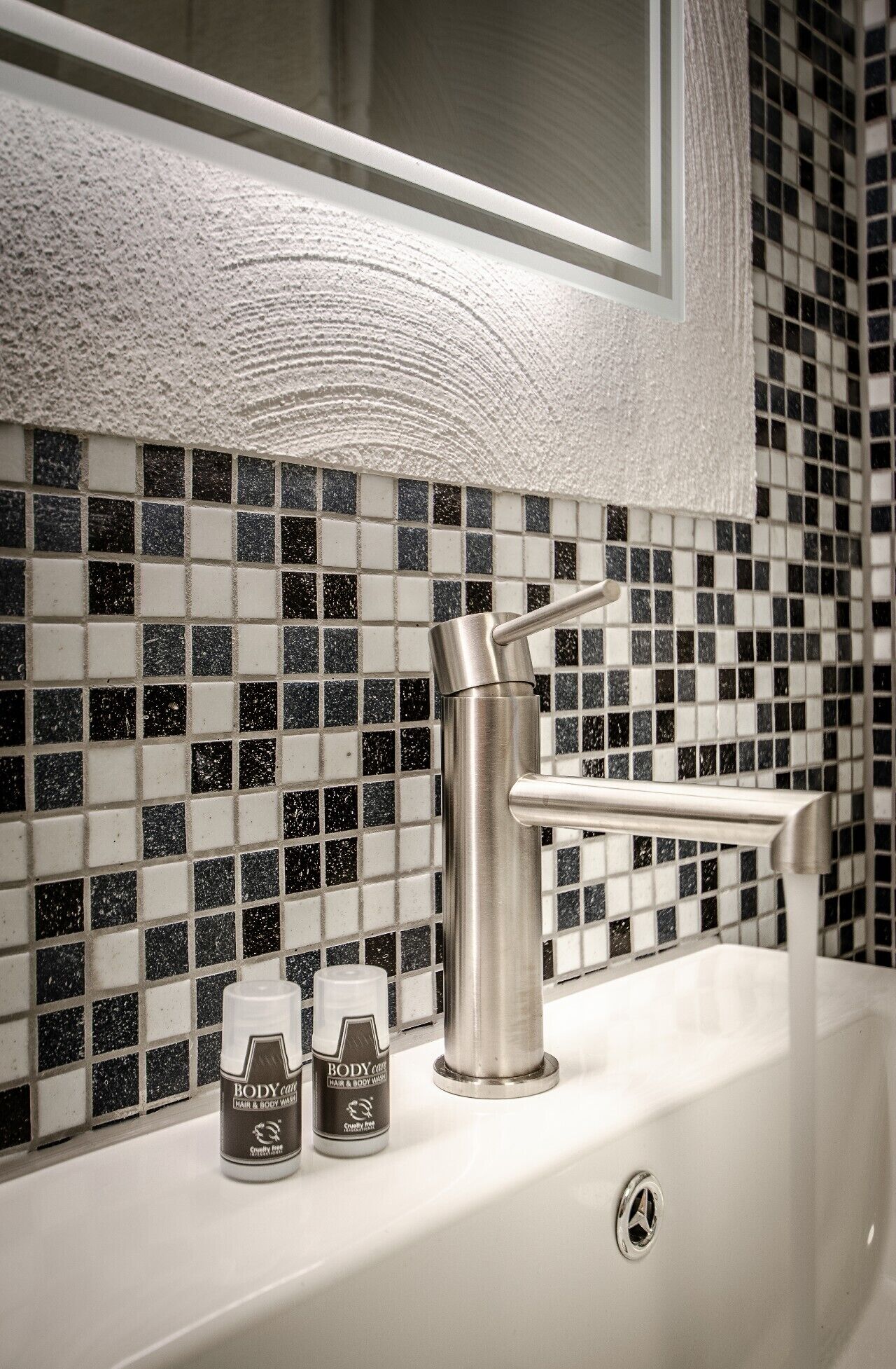 A bathroom with a white sink, a modern faucet, and a tiled backsplash with black and white tiles.