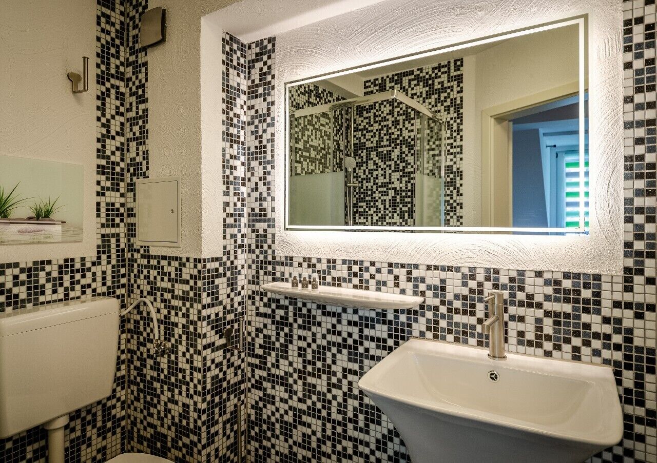 Ein Badezimmer mit Wänden aus schwarz-weißen Mosaikfliesen, einem weißen Waschbecken und einem Spiegel darüber.
