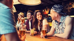 Eine Gruppe von Menschen sitzt an einem Holztisch in einer Bar und hält Biergläser.