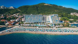 Een hotel met een zwembad en een strandgedeelte, omgeven door bergen en een waterpartij.