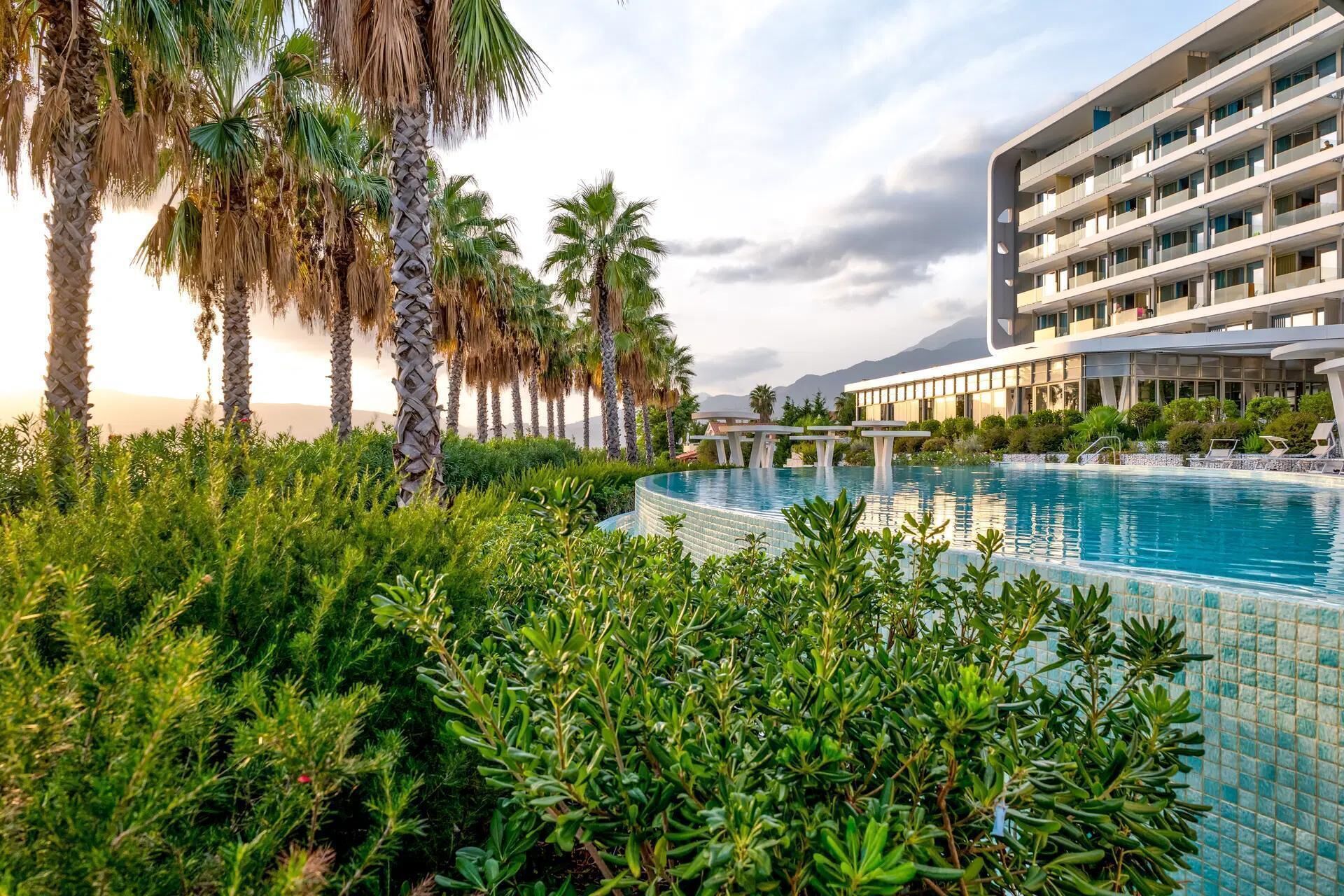 Ein Pool, umgeben von üppiger Vegetation und Palmen, mit einem modernen Gebäude im Hintergrund.