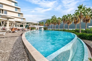 A swimming pool with lounge chairs and palm trees, surrounded by a building with a modern design.