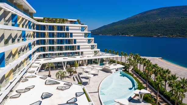 Een modern hotel met een zwembad, ligbedden en uitzicht op zee.