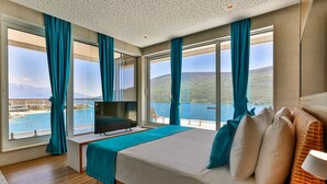 Hotelkamer met een groot bed, een televisie en uitzicht op water en bergen.