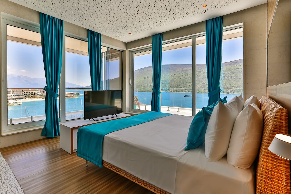 Une chambre d’hôtel avec un grand lit, une télévision et une vue sur un plan d’eau et des montagnes.