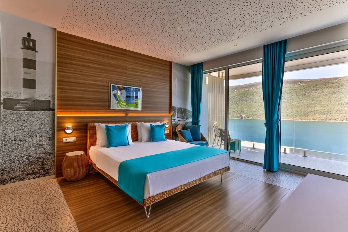 Une chambre d’hôtel moderne avec un grand lit, une vue sur l’eau et un balcon équipé d’une chaise.