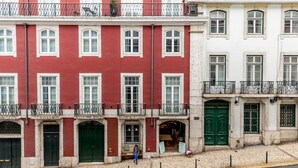 A row of red and white buildings with balconies, green doors, and a cobblestone street. - LeL Madalena GuestHouse (Lisbon)
