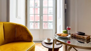 A room with a yellow armchair, a table with a plate of food, a glass of red drink, an apple, and a book. - LeL Madalena GuestHouse (Lisbon)