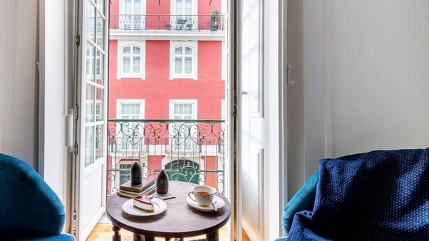 A balcony with a table, a chair, and a view of a red building. - LeL Madalena GuestHouse (Lisbon)