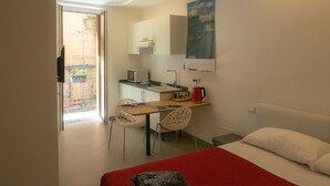 A compact hotel room with a bed, a small kitchenette, a dining area, and a view of the outside balcony. - San Francesco Rooms L.T. (Palermo)