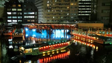 Un barco fluvial iluminado con varios niveles y una cubierta superior cubierta, rodeado de edificios con ventanas iluminadas de noche.