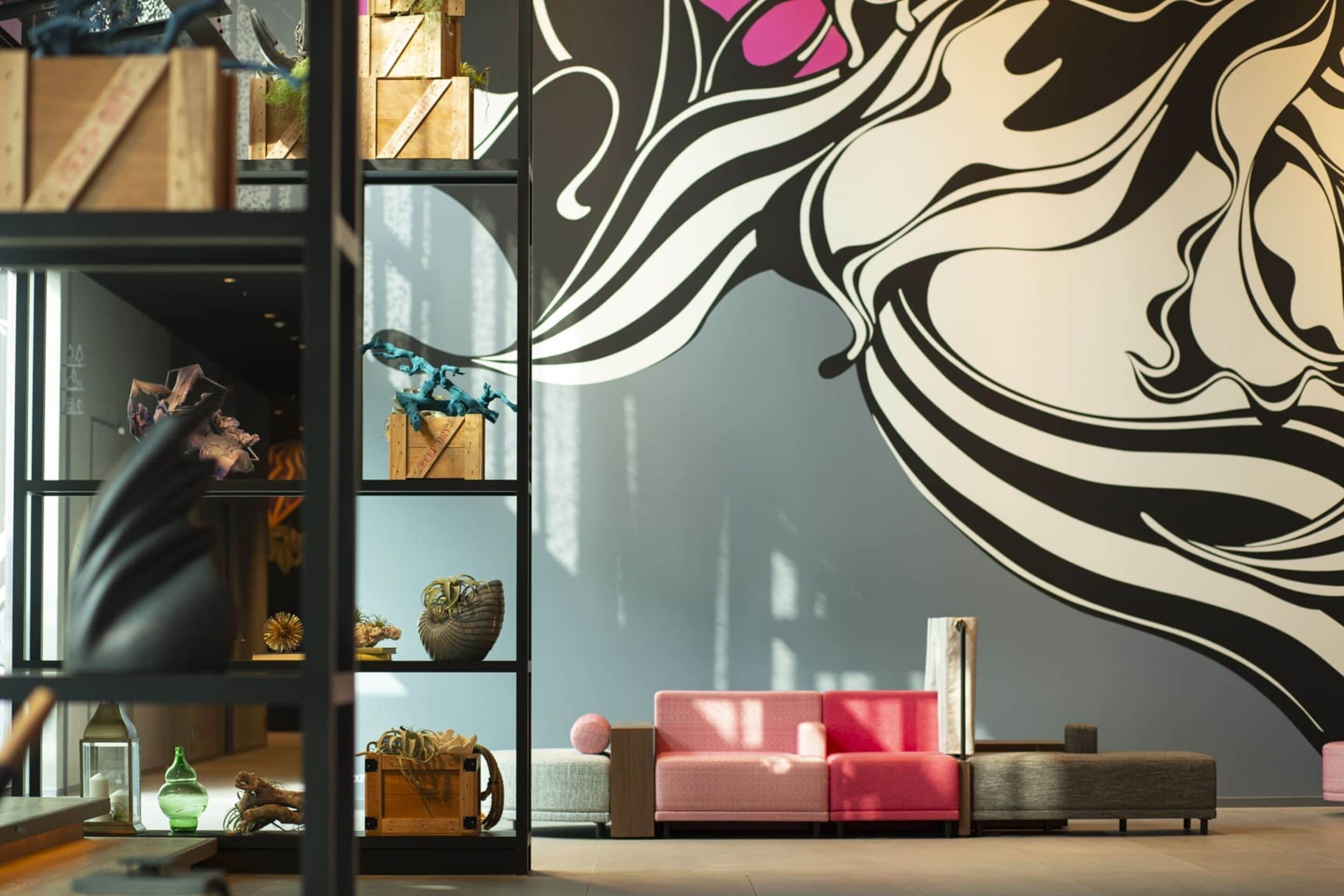 Un interior moderno con un gran mural abstracto, una estantería de madera y un sofá rosa.