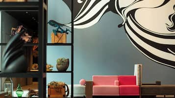 A modern interior with a large abstract mural, a pink sofa, and a wooden shelf unit with various decorative items.