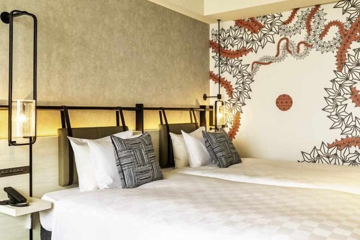 Quarto de hotel com cama, luminárias de cabeceira, telefone e parede com padrão de folhas.