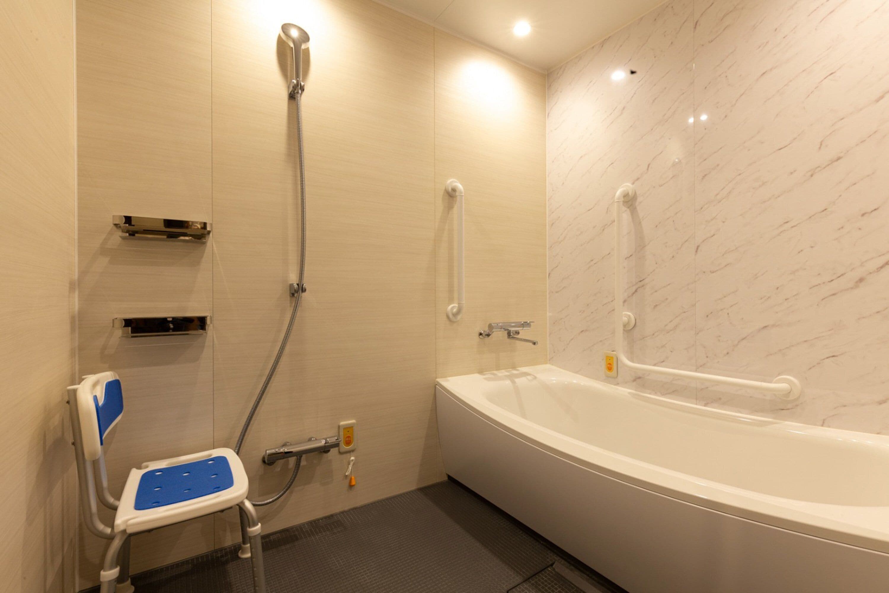 A bathroom with a white bathtub, a shower with a handheld showerhead, a grab bar, and a wheelchair-accessible seat.