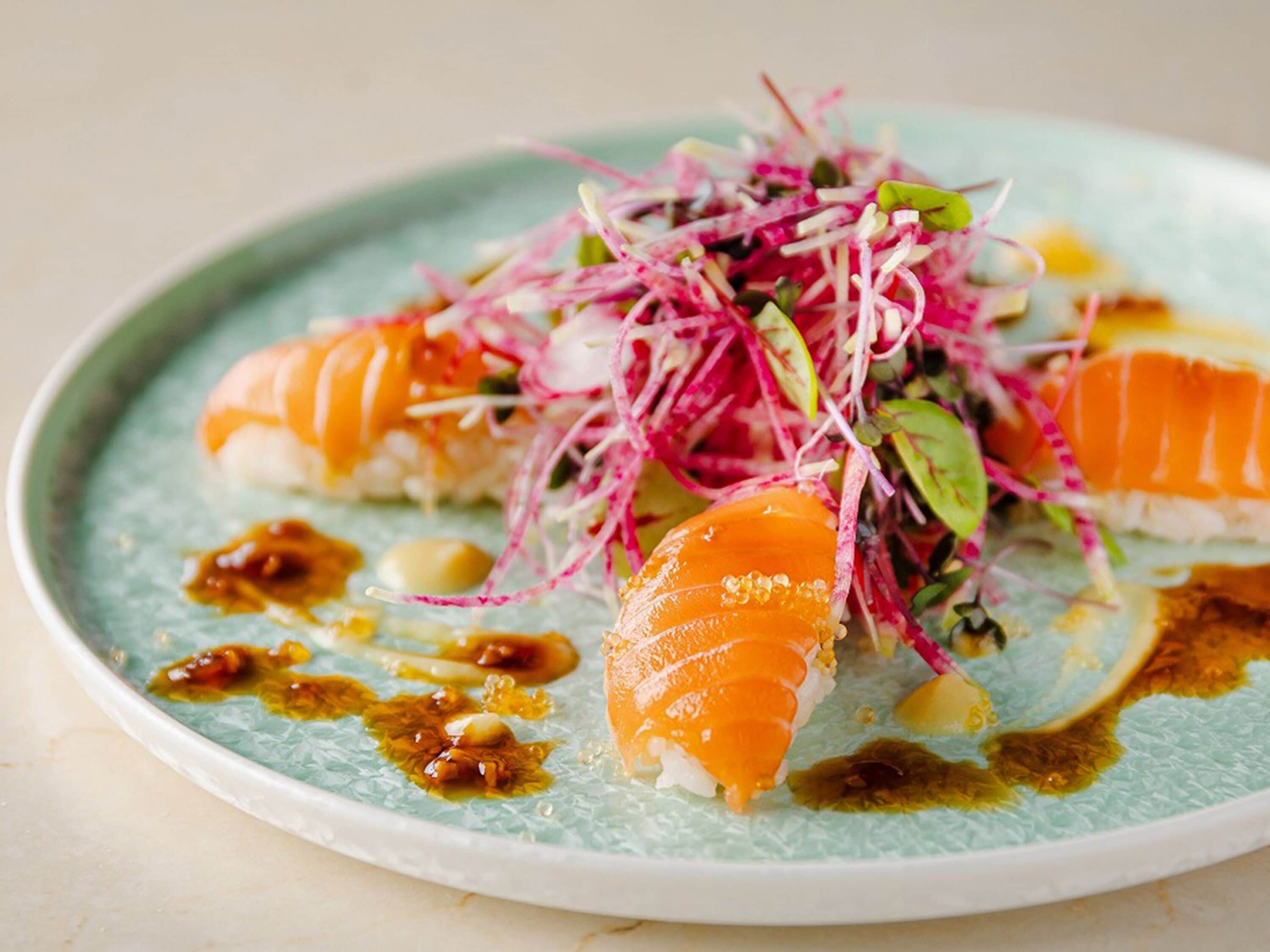 A plate of sushi with a garnish of shredded vegetables and a drizzle of sauce.